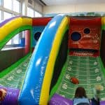 Two children play a football toss game, aiming at target holes on an inflatable, colorful arcade with yard lines and sports-themed decorations—perfect for party rentals Long Island or bounce house fun in NY.