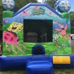 A SpongeBob SquarePants-themed bounce house, available for party rentals Long Island, features images of SpongeBob, Patrick, and Squidward. Set outdoors on grass with trees and a cloudy NY sky in the background.