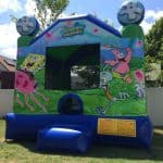 A SpongeBob SquarePants-themed inflatable bounce house is set up on a grassy lawn in NY, available through party rentals Long Island, featuring images of SpongeBob, Patrick, and Squidward catching jellyfish with blue sky and trees in the background.