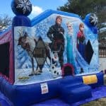 A blue and purple Frozen-themed bounce house Long Island features large images of Sven, Kristoff, Olaf, Elsa, and Anna with snowflake decorations. Perfect for party rentals Long Island, it’s being set up on a lawn.