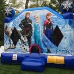 A blue inflatable bounce house Long Island decorated with Disney’s Frozen characters—Kristoff, Elsa, Anna, Sven, and Olaf—set up on grass with white chairs nearby; perfect for party rentals Long Island, NY.