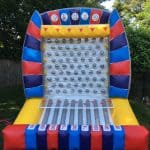 An inflatable Plinko game with colorful red, blue, and yellow sections, perfect for party rentals Long Island, NY—featuring a peg grid and numbered slots, set up outdoors on grass for endless fun.