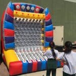 Two children stand in front of a large, colorful inflatable Plinko game board outdoors at a NY event, preparing to drop disks down the peg-filled surface—just one of many fun attractions from party rentals Long Island offers.