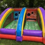 A colorful inflatable football toss game with two lanes, each featuring a target hole and yard line markings, set outdoors on green grass—perfect for NY party rentals Long Island events with trees in the background.