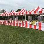 Red and white striped tents set up outdoors on grass with tables underneath, serving food like hot dogs and hamburgers—perfect for an NY event. Ideal for parties with party rentals Long Island or even a bounce house Long Island for extra fun!.