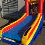 An inflatable basketball game with a slide, featuring bright red, yellow, and blue colors, is set up outdoors near a basketball hoop and a building—perfect for NY parties from party rentals Long Island.