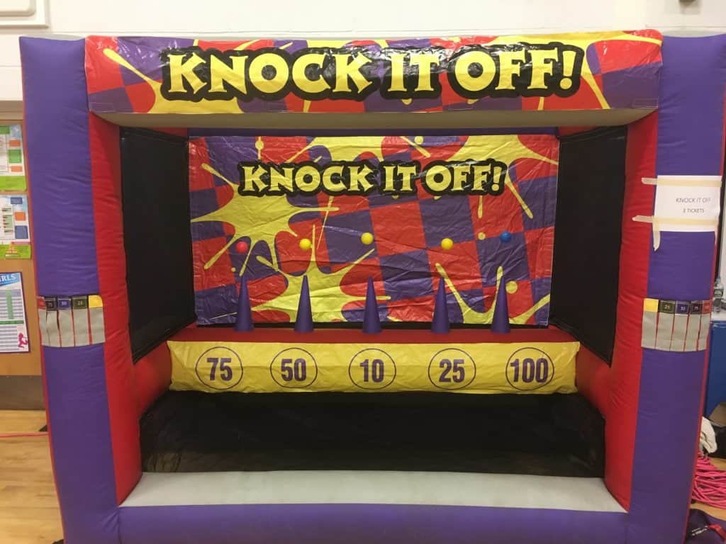 Inflatable carnival game booth labeled "Knock It Off!" with targets showing scores of 75, 50, 10, 25, and 100, plus five blue cones inside—perfect for party rentals Long Island and fun events across NY.