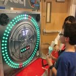 A boy holding blue cotton candy stands in front of a vault-themed arcade game with green and red lights at a party rentals Long Island event, while another person stands behind him. The game display reads, "You have 30 seconds.