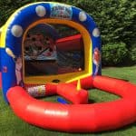 An inflatable baseball game with a red and blue structure, baseball graphics, and targets inside, set up on a green lawn with trees in the background—perfect for party rentals Long Island or bounce house fun in NY.
