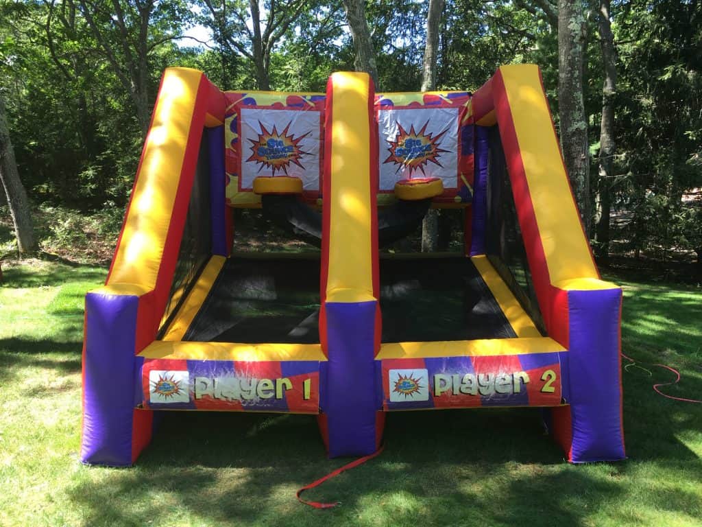 Inflatable basketball game with two side-by-side lanes labeled "Player 1" and "Player 2," each with a basketball hoop and colorful decorations, set outdoors on grass—perfect for NY parties or bounce house Long Island rentals.