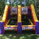 Inflatable basketball game with two side-by-side lanes labeled "Player 1" and "Player 2," each with a basketball hoop and colorful decorations, set outdoors on grass—perfect for NY parties or bounce house Long Island rentals.