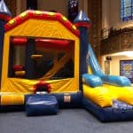 A colorful inflatable bounce house with a slide is set up indoors on blue carpet, surrounded by stained glass windows and ornate decor—perfect for party rentals Long Island, NY.