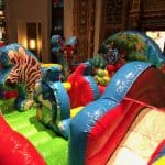 Colorful indoor inflatable play structure with jungle animal designs, including a zebra, deer, and owl. Perfect for NY party rentals Long Island, it features a bouncy surface and slide surrounded by ornate walls and stained glass windows.