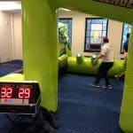 A digital scoreboard shows scores of 32 and 29 in front of a bounce house Long Island setup, with children playing inside and stained glass windows providing a vibrant backdrop.