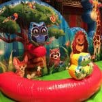 Colorful inflatable play area decorated with cartoon animals—including an owl, lion, raccoon, and more—set against a backdrop of trees and greenery; perfect for party rentals Long Island or those seeking a unique bounce house Long Island, NY.