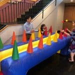Four people gather around an inflatable table with colorful traffic cones and floating balls, enjoying a lively game indoors near a staircase—perfect inspiration for party rentals Long Island events.