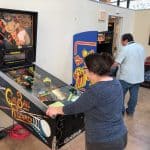A woman plays a Cue Ball Wizard pinball machine while a man enjoys Pac-Man in a game room filled with other arcade machines—perfect inspiration for party rentals Long Island, NY, or pairing with a bounce house Long Island for added fun.