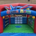 Colorful inflatable “Game Zone” play structure featuring tic-tac-toe and toy box themes, with bright red, blue, and green panels—perfect for party rentals Long Island, NY—set up outside near a building wall.