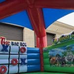 Inflatable play structure with Tic Tac Toe and Puzzle game panels, featuring animal illustrations like zebras, giraffes, and lions—perfect for outdoor fun near a tan building with garage doors. A favorite among bounce house Long Island party rentals!.