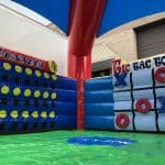 A large inflatable game setup by bounce house Long Island features Connect 4 on the left and Tic Tac Toe on the right, both with colorful designs, under a canopy on a green, padded surface—perfect for NY party rentals.