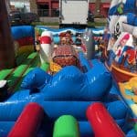 Colorful inflatable pirate-themed bounce house Long Island featuring cartoon pirate characters, a ship, shark, palm trees, barrels, cannons, and soft obstacles. The structure is set up outdoors on a sunny day—perfect for NY party rentals Long Island.