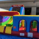 A colorful inflatable obstacle course called "Radical Run II," featuring slides, tunnels, and climbing areas, set up outdoors on a blue tarp in front of a building—perfect for party rentals Long Island events.