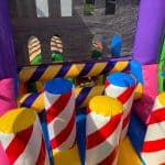 Colorful inflatable obstacle course with vertical pillars in red, yellow, white, blue, and purple stripes. Perfect for NY parties, this bounce house Long Island rental features bright colors and a safe mesh wall at the back.
