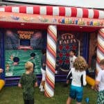 Children play in front of an inflatable carnival games booth, featuring “Touchdown Toss” and “Star Darts,” with colorful graphics. Perfect for parties, these outdoor games are popular choices for party rentals Long Island, NY families love.