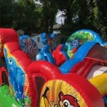 Colorful inflatable bounce house Long Island with cartoon animal designs, including a zebra, deer, and tiger, set up outdoors on green grass with trees and a white fence—perfect for NY party rentals Long Island.