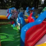 Colorful inflatable bounce house Long Island with animal-shaped obstacles, including a zebra and reindeer, set up outdoors on green grass—perfect for NY party rentals with a white fence and trees in the background.