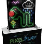 Large electronic game display titled "PIXEL PLAY" features a pixelated green dinosaur, red ball, and white cloud. Perfect for party rentals Long Island, the black console below is labeled "PIXEL PLAY" in colorful dots.