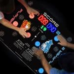 Two people play a fast-paced, hand-slapping arcade game on a light-up table—an exciting addition to any party rentals Long Island event—with red and blue score displays and illuminated “Player 1” and “Player 2” buttons.