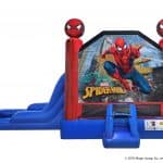 A blue and red inflatable bounce house Long Island features Spider-Man graphics, two 3D Spider-Man heads on top, and an attached slide on the left. The front shows Spider-Man swinging through a city—perfect for party rentals Long Island, NY!.