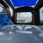 View from inside a bounce house Long Island, showing shiny, padded floor and blue climbing wall. Outside, a light blue house, red vehicle, and trees are visible through the mesh walls—perfect for NY party rentals Long Island events.