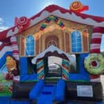 A colorful inflatable bounce house designed like a candy-themed gingerbread house, featuring candy canes, lollipops, donuts, and ice cream decorations—perfect for party rentals Long Island, NY under a bright blue sky.