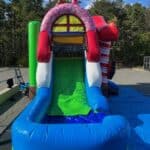 A colorful inflatable slide with ice cream and candy decorations, featuring a bright green sliding area and blue padded sides, perfect for NY parties and available from bounce house Long Island party rentals, set outdoors on a sunny day with trees in the background.