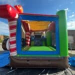 An inflatable bounce house with red, white, green, and brown colors stands outdoors on a blue tarp, perfect for party rentals Long Island. Clear sky and buildings can be seen in the background.