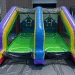 An inflatable soccer-themed game with two goals and two illustrated goalkeepers, set up outdoors in NY, perfect for party rentals Long Island, right in front of a building with two large garage doors.