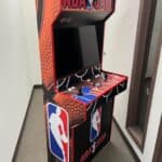 An NBA Jam arcade cabinet with a basketball-themed design, joysticks, buttons, and a large screen—perfect for party rentals Long Island. Features the NBA logo and "NBA Jam" branding on the front and sides.