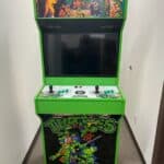 A Teenage Mutant Ninja Turtles arcade machine with a green frame and colorful TMNT graphics, featuring two joysticks and multiple buttons, stands in a hallway—perfect for NY party rentals or bounce house Long Island events.