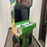 An upright Teenage Mutant Ninja Turtles arcade machine with vibrant green trim, colorful graphics, dual joysticks, and buttons stands in a narrow hallway—perfect for party rentals Long Island or NY events.