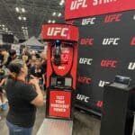 At an indoor NY event, a woman stands before the Boxing Machine Arcade Game, ready to test her strength. Surrounded by spectators and excitement, it’s the perfect highlight for party rentals Long Island style.