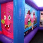 Inside a vibrant bounce house Long Island kids love, with blue and purple walls, a cartoon pink monster, colorful mountains, and a playful “WANTED! $1 REWARD!” poster—perfect for NY party rentals Long Island events.