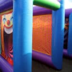 Brightly colored inflatable carnival game structure, featuring a large clown face on one panel and a wall of red and yellow dots on another, with blue and green inflatable supports—perfect for bounce house Long Island party rentals.
