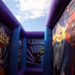View from inside an inflatable carnival-themed maze, offered by party rentals Long Island, with colorful cartoon banners on the walls and a bright blue sky with clouds visible above.