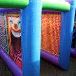 An inflatable maze on Long Island features bright blue and green columns, a smiling clown face, and vibrant patterns—perfect for NY party rentals or pairing with a bounce house Long Island event.