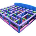 Large inflatable maze with colorful purple, blue, pink, and green walls and pathways—perfect for party rentals Long Island, NY. Surrounded by inflatable barriers and featuring an open top, it's designed for guests to walk through and enjoy.