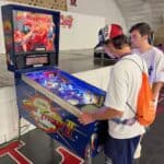 Two young men play a Super Street Fighter II pinball machine inside an arcade. The colorful machine lights up the room, perfect inspiration for party rentals Long Island, NY, where fun and excitement are always on offer.