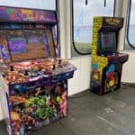 Two arcade game machines stand side by side—one with Marvel superheroes artwork, the other a classic Pac-Man. Perfect for indoor fun or party rentals Long Island, they're set by large windows for a vibrant atmosphere.