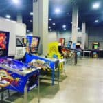 A row of colorful arcade and pinball machines, including Street Fighter II and Road Show, are set up in a spacious indoor area with concrete floors and large pillars—perfect for party rentals Long Island, NY. A van is parked on the left.